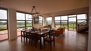 A spacious dining area with a wooden table and chairs, large windows offering a view of the outdoors, and a staircase leading to an upper level. - Crown Hotel Palawan at Harbour Springs (Puerto Princesa)