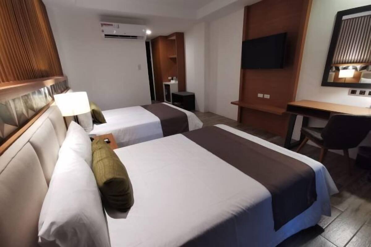 Ein Hotelzimmer mit zwei Betten, einem Schreibtisch, einem Stuhl, einem Fernseher und einem Spiegel.