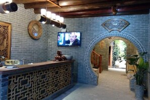 A reception area with a patterned counter, a television mounted on the wall, and an arched doorway leading to another room. - Huangyao Ancient Town (Zhaoping)