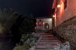 Edificio tradicional con escalones de piedra que conducen a una puerta, rodeado de vegetación e iluminado por luces empotradas.