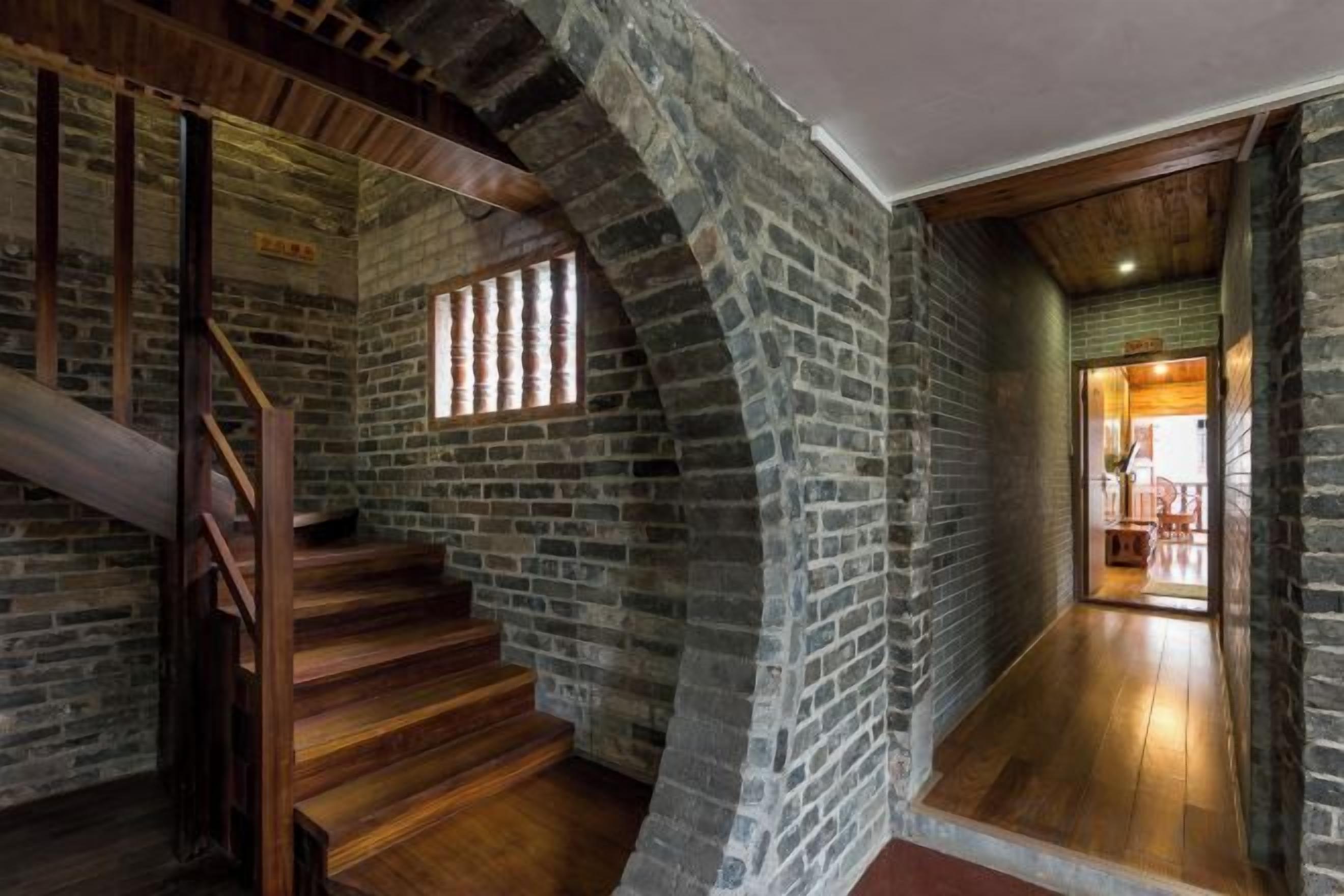 Un escalier avec des marches en bois et un mur en briques, menant à une pièce dotée d’un plancher en bois et d’une fenêtre.