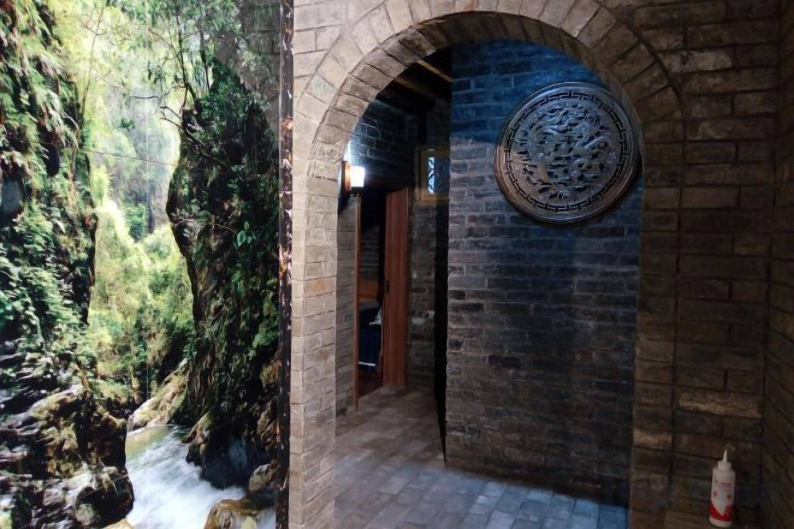 An arched brick corridor with a circular wall decoration and a view of a rocky outdoor area.