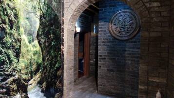 An arched brick corridor with a circular wall decoration and a view of a rocky outdoor area.
