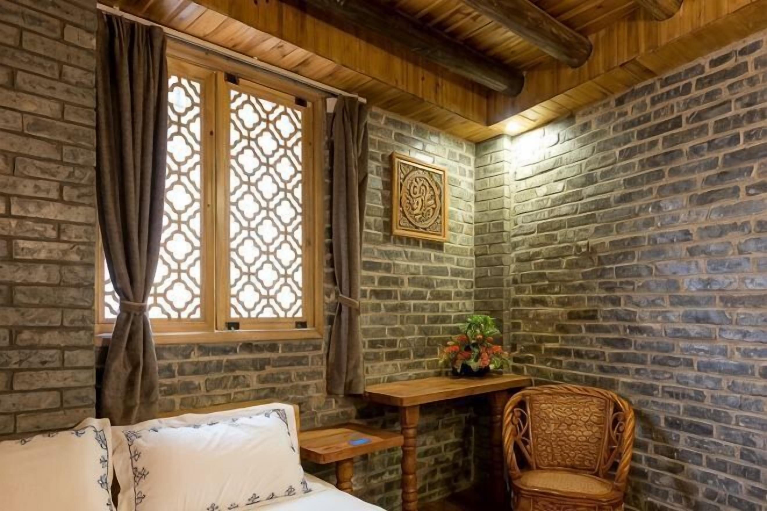 A room with a bed, a wooden desk, a wicker chair, and a decorative wall piece.