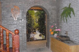Un arco de piedra que da acceso a un espacio con un mural de cascada, una escalera de madera y una planta en un estante.