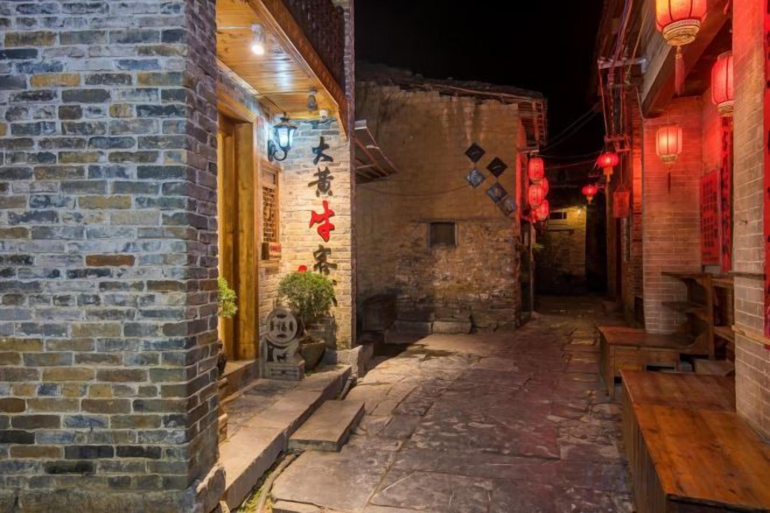 Un estrecho callejón con edificios de ladrillo tradicional, bancos de madera y faroles rojos.