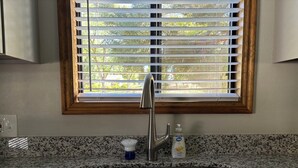 A kitchen with a stainless steel sink, a window with blinds, and a countertop with a soap dispenser.