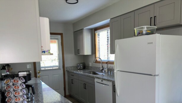 A kitchen with granite countertops, a refrigerator, a dishwasher, and cabinets.