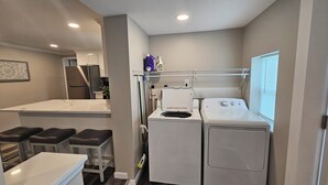 A compact kitchen with a refrigerator, washing machine, and a small dining area with stools.