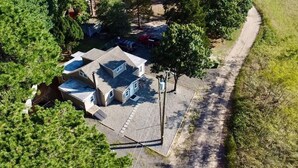 An aerial view of a residential property with a detached house, a paved driveway, and surrounding greenery.