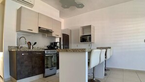 Una cocina moderna con horno empotrado, cafetera y refrigerador. Hay tres taburetes de bar y un estante pequeño sobre la encimera.