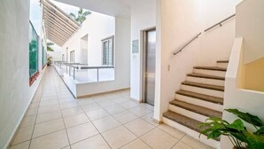 Un couloir avec un escalier, un sol carrelé et une rambarde.