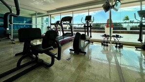 Ein Fitnessstudio mit Trainingsgeräten, großen Fenstern und Blick auf Palmen.
