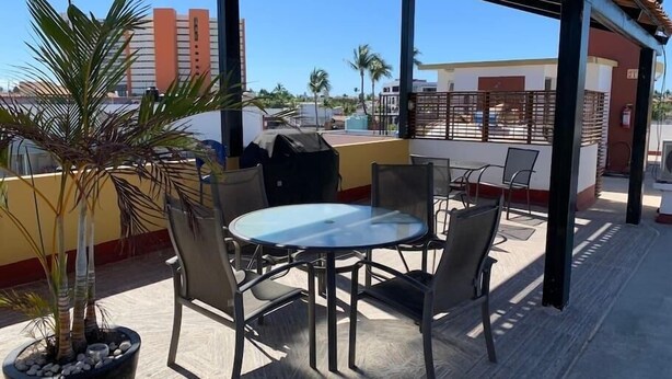 En tagterrasse med et rundt bord, stole, en potteplante og en grill.
