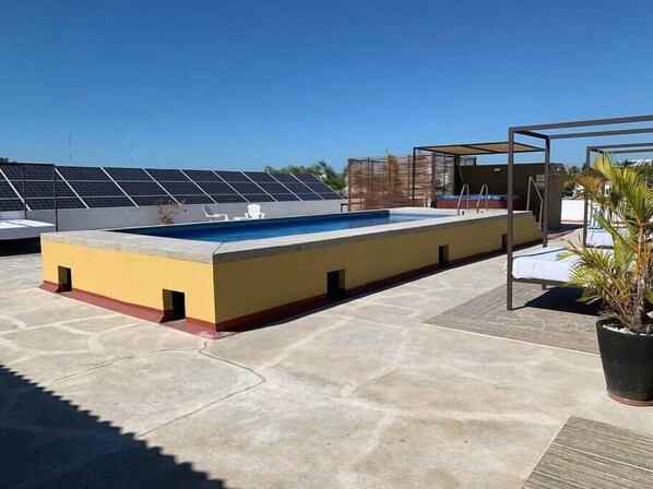 Une piscine sur le toit, dotée de panneaux solaires, un espace salon couvert et des plantes en pot.