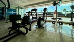 Ein Fitnessraum mit Trainingsgeräten, großen Fenstern und Blick auf Palmen.
