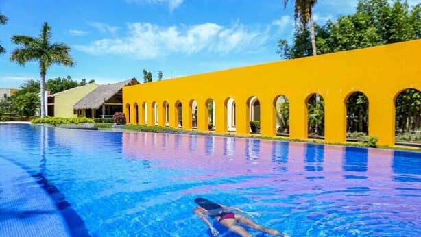 A swimming pool with a person swimming, surrounded by a yellow building with arched windows. - Wellness apartment | Golf Club, pool and spa (Nuevo Vallarta)