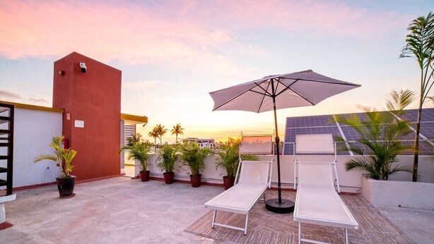 Une terrasse sur le toit, avec deux chaises longues, un grand parasol et des plantes en pot.