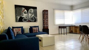 Un salon moderne avec un canapé bleu, une table basse blanche et un grand tableau abstrait.
