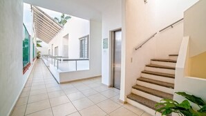Un couloir propre et moderne, avec un escalier, un sol carrelé et une vue sur l’extérieur.