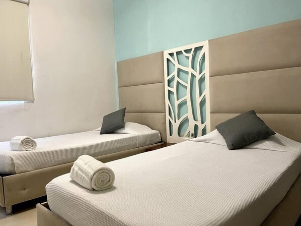Deux lits simples avec des têtes de lit, un séparateur de pièce et une fenêtre avec des stores.
