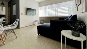 A modern living room with a dark sofa, a white coffee table, and a TV mounted on the wall.
