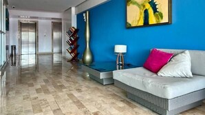 Un vestíbulo moderno con una pared azul de acento, un cuadro abstracto de gran tamaño, un jarrón alto, una lámpara de pie y un sofá blanco con un cojín rosa.