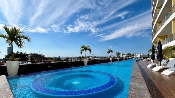Una piscina de diseño circular, rodeada de tumbonas y palmeras, con un cielo despejado al fondo.