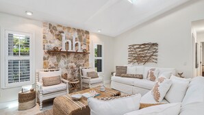 Un salón amplio con una pared de acento de piedra, muebles blancos y una mesa de centro tejida.