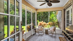 Un patio cubierto con ventanas amplias, un ventilador de techo y una parrilla.