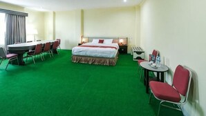 A hotel room with a bed, a desk with chairs, a small table, and a green carpet. - RedDoorz @ Brother Homestay Kupang (Kupang)