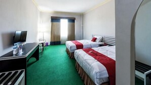 A hotel room with two beds, a desk with a TV, a small table, and a window with curtains. - RedDoorz @ Brother Homestay Kupang (Kupang)