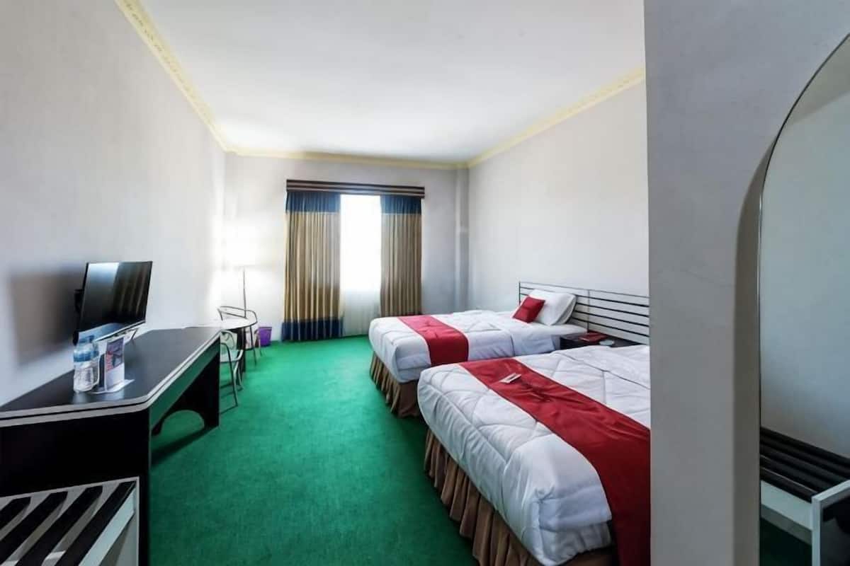 Quarto de hotel com duas camas, uma escrivaninha com televisão, uma mesinha e uma janela com cortinas.