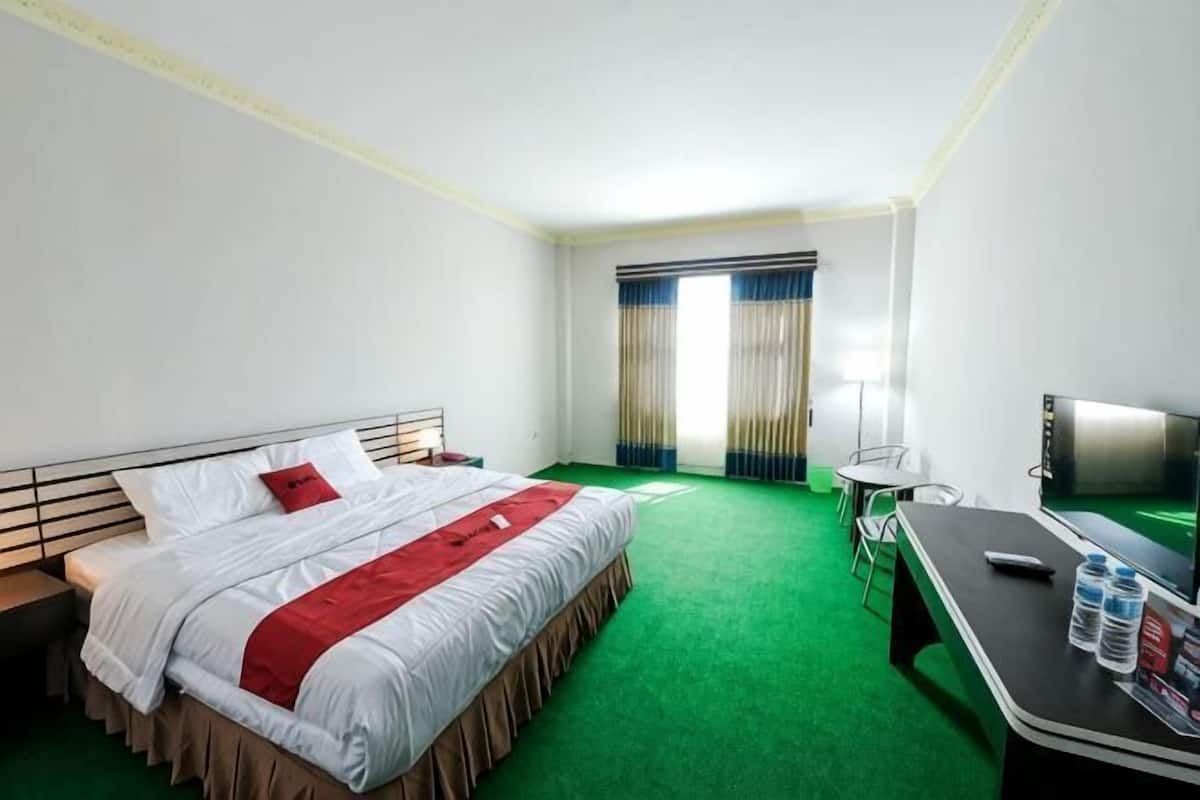 Quarto de hotel com cama, escrivaninha, televisão e janela com cortinas.
