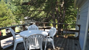 Eine Holzterrasse mit einem runden Tisch und vier weißen Stühlen.