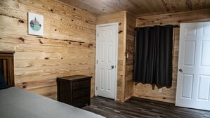 Ein Zimmer mit Holzwänden, einem Bett, einer Kommode und zwei Türen.
