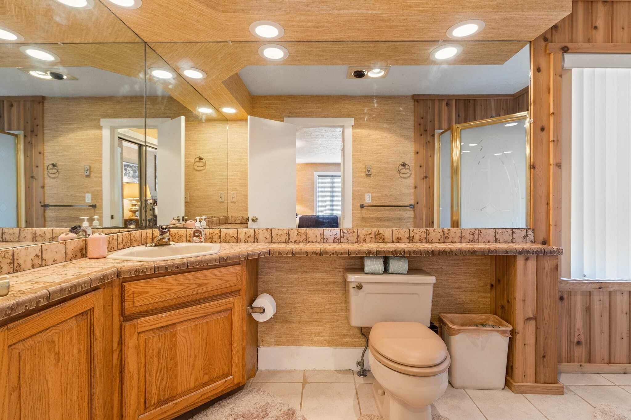A bathroom with wooden paneling, a marble countertop, a sink, a toilet, and a mirror.