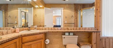 A bathroom with wooden paneling, a marble countertop, a sink, a toilet, and a mirror.