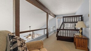 A loft bedroom with a wooden staircase, a sofa, a small table, and a lamp.