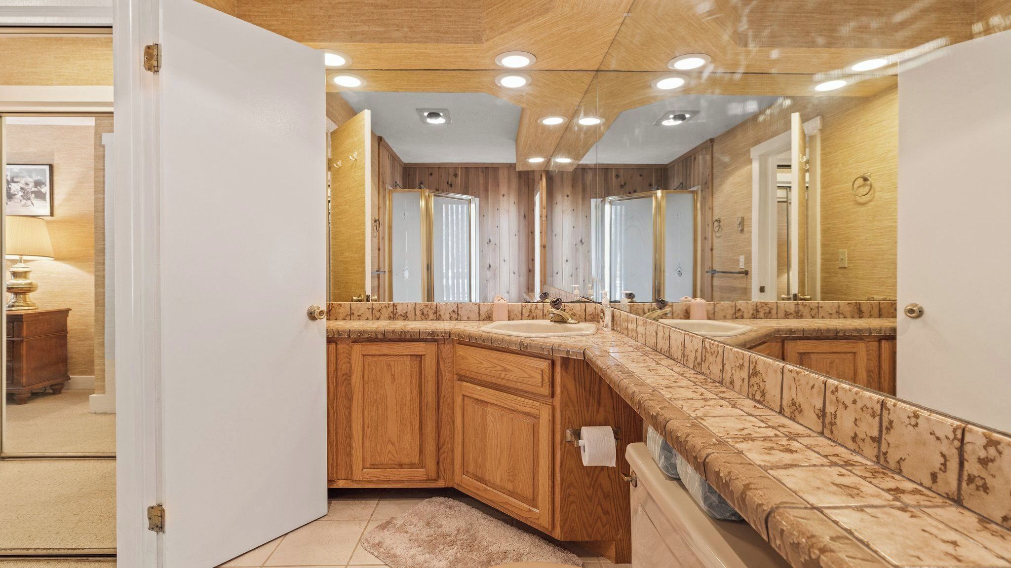 Une salle de bain avec des meubles en bois, un comptoir en marbre et un grand miroir.