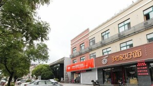 Gadesyn med en bygning, et skilt på et fremmedsprog, en parkeret bil og et træ.