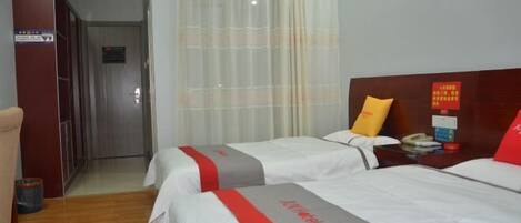 A hotel room with two beds, a wooden wardrobe, a curtain, and a nightstand with a phone and a red pillow.