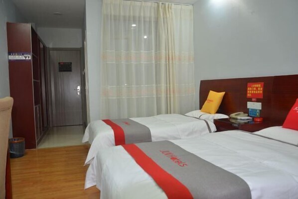 A hotel room with two beds, a wooden wardrobe, a curtain, and a nightstand with a phone and a red pillow. - Shenzhou Business Hotel (Jinhu)