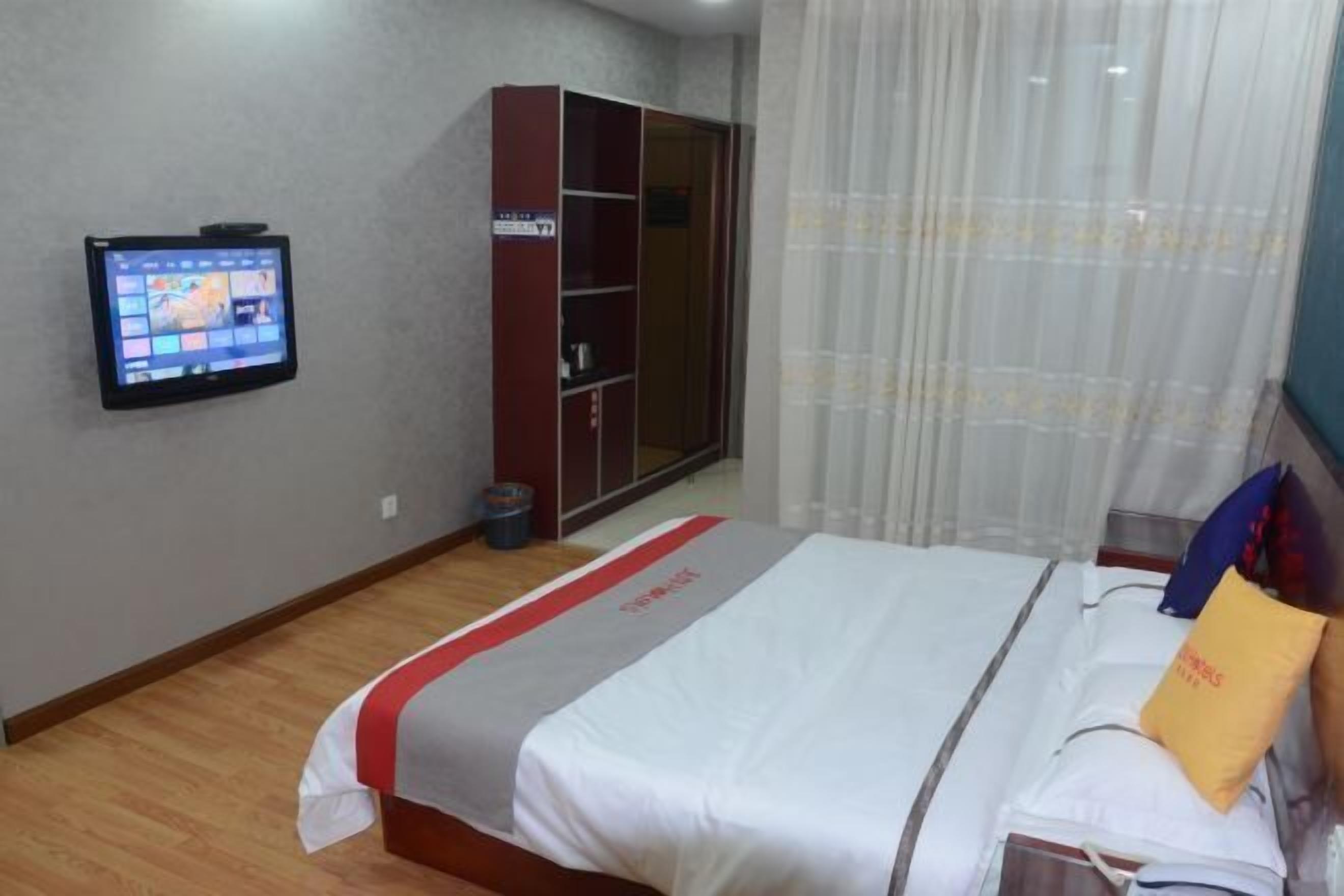 Una habitación de hotel con cama, televisor montado en la pared, armario y cortina.