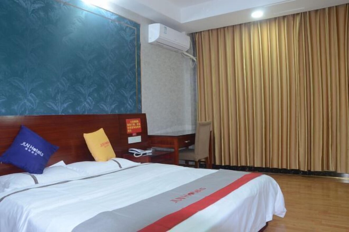 A hotel room with a bed, a desk, an air conditioning unit, and a curtain.