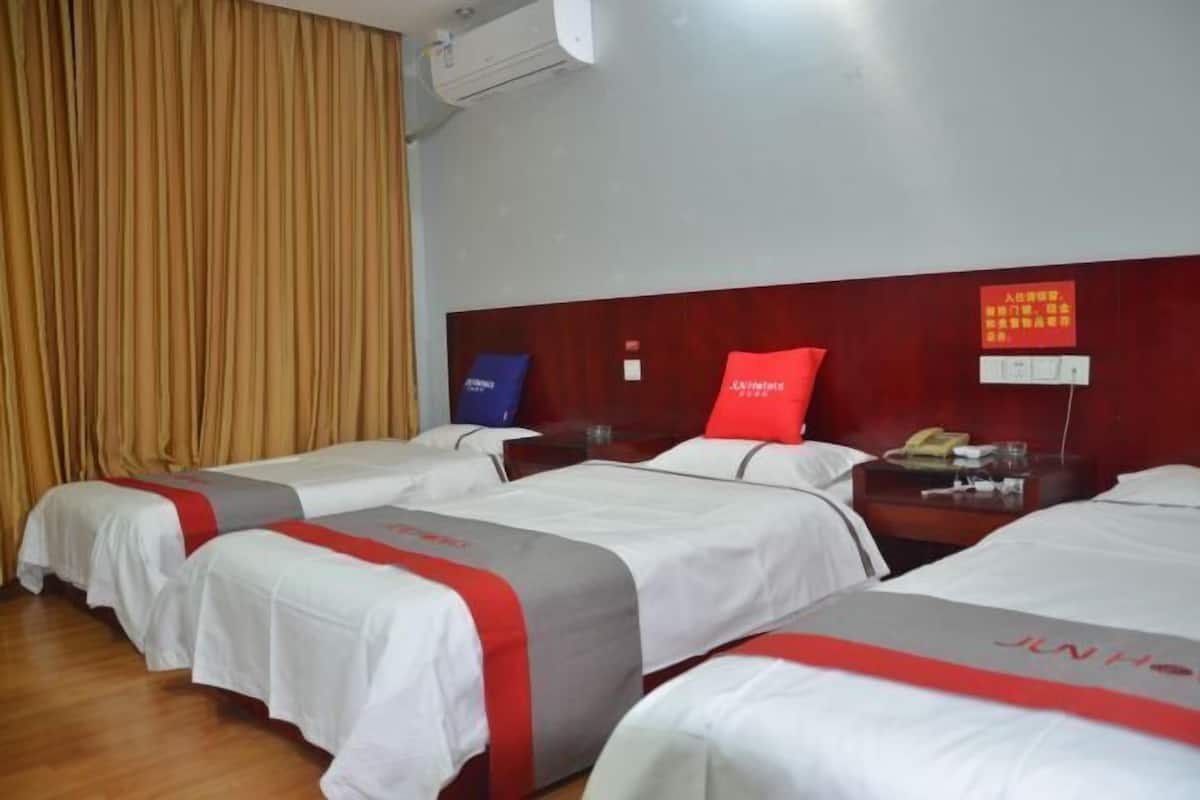 A hotel room with four beds, each with a white and red bedspread, a wooden headboard, and a red pillow. There is a wooden nightstand with a telephone and a glass of water.