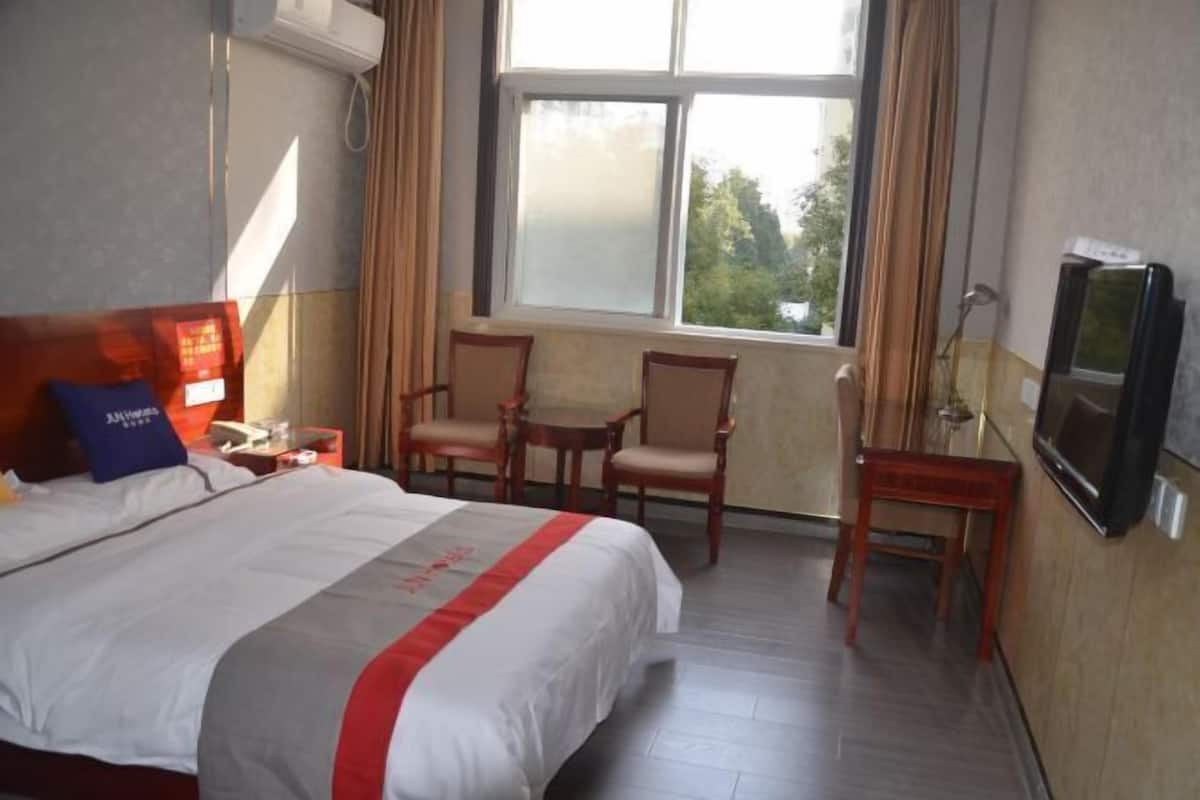 A hotel room with a bed, two chairs, a small table, a TV, and a window with curtains.