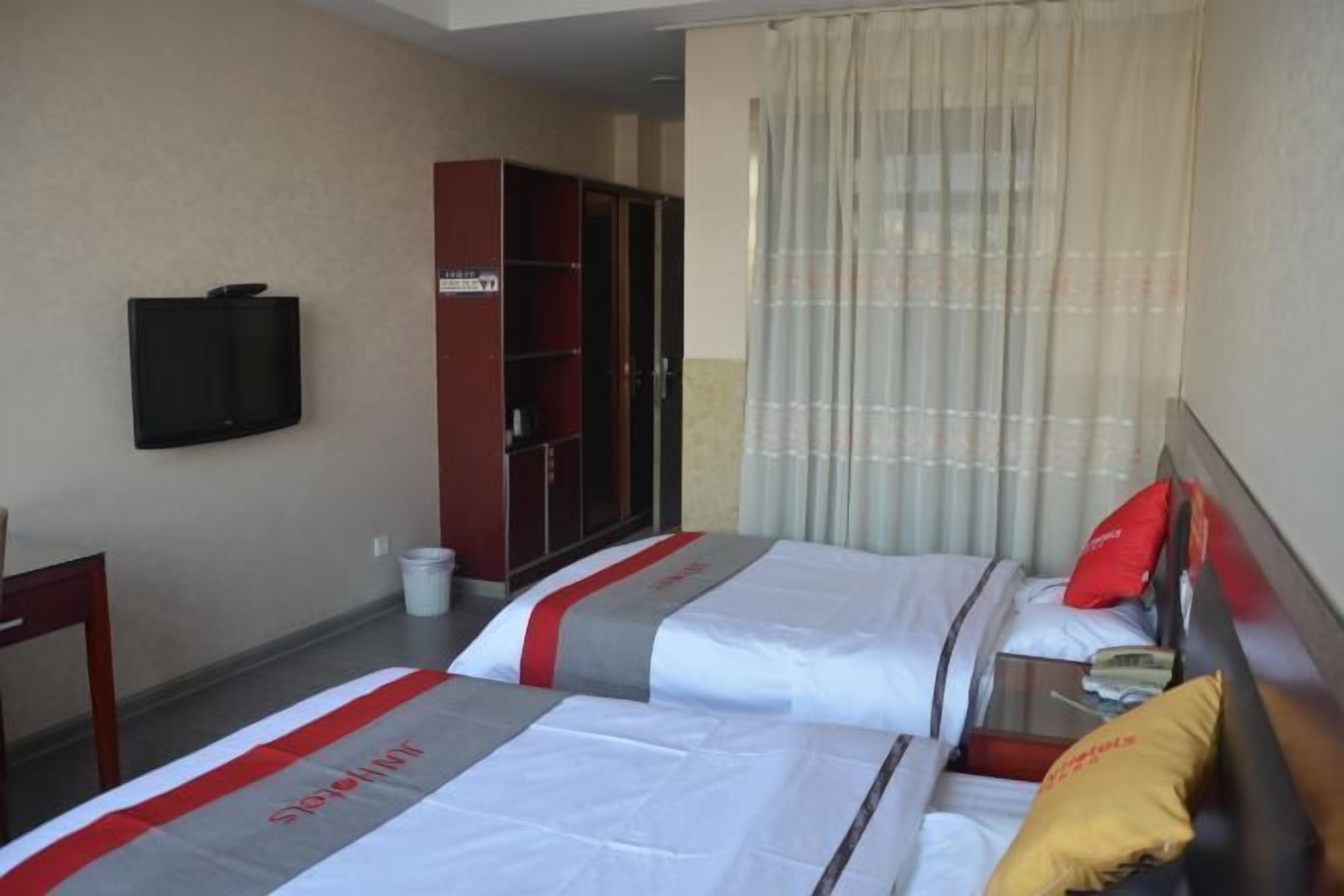 A hotel room with two beds, a television, a wardrobe, and a curtain.