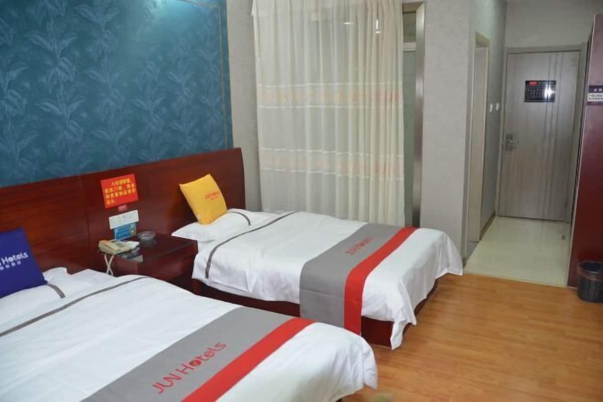 A hotel room with two beds, a wooden headboard, a nightstand, a telephone, and a window with curtains.