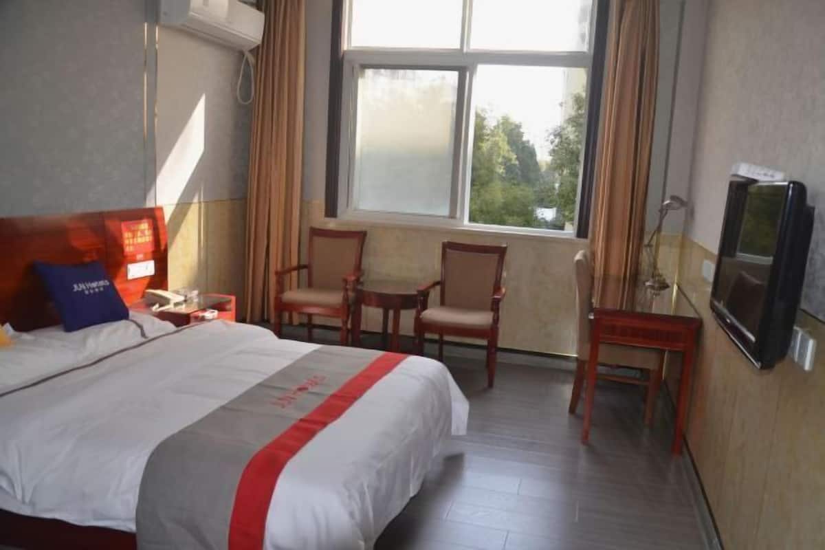 A hotel room with a bed, two chairs, a small table, a TV, and a window with curtains.
